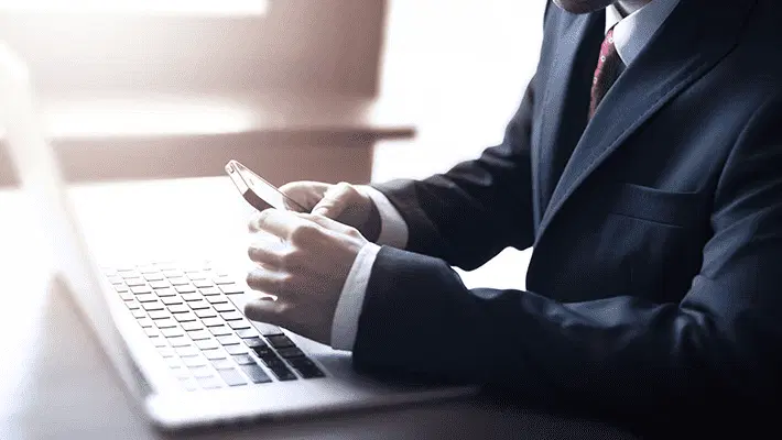 hombre manipulando un teléfono móvil iOS delante de un ordenador