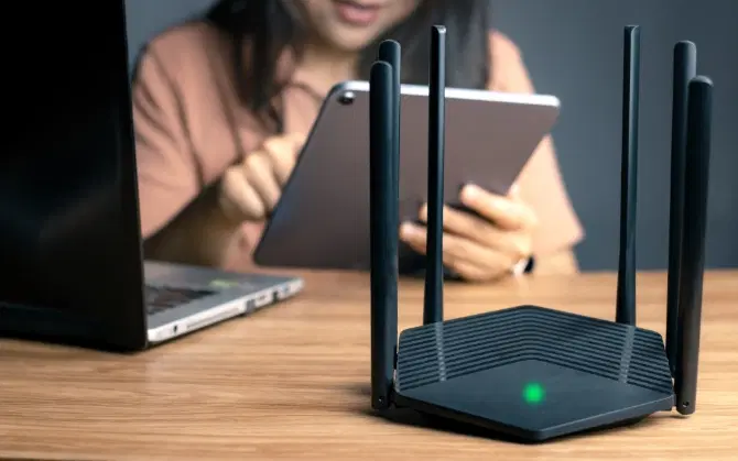 Nahaufnahme eines Internet-Routers auf einem Arbeitstisch mit verschwommenem Hintergrund mit einer Frau, die ein Tablet verwendet