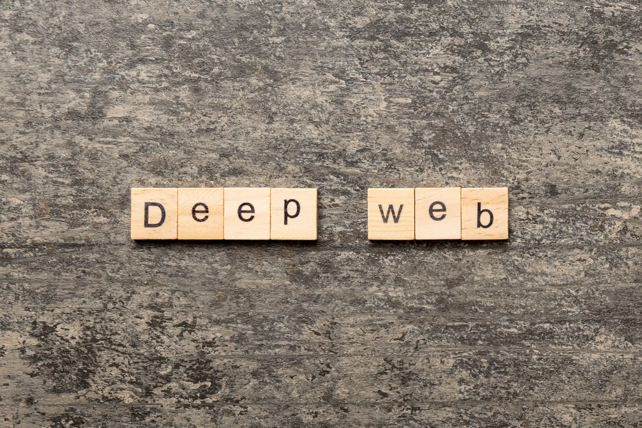 Bogstavfliser af træ, der staver "Deep Web" på en tekstureret grå baggrund.