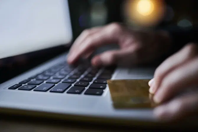 A hacker in a dark room with a laptop, holding a credit card