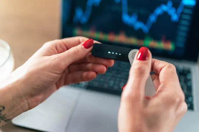 Eine Person hält eine digitale Geldbörse für Kryptowährungen vor einem Laptop in der Hand
