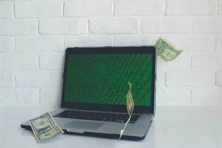 Hakkeroitu kannettava, jonka ympärillä leijuu dollarin seteleitä Hakkeroitu kannettava, jonka ympärillä leijuu dollarin seteleitä