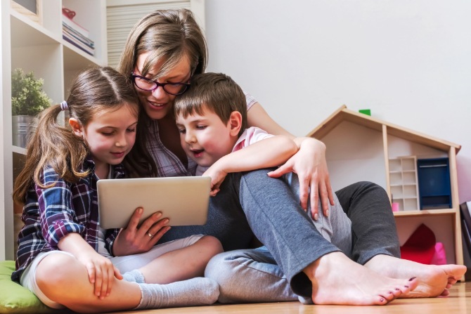 A parent and two children looking at a tablet