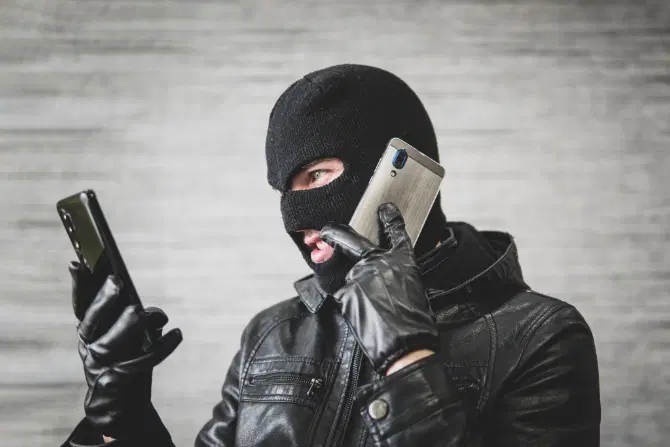 adult in black clothing with a hidden face, using a mobile phone for fraudulent activity