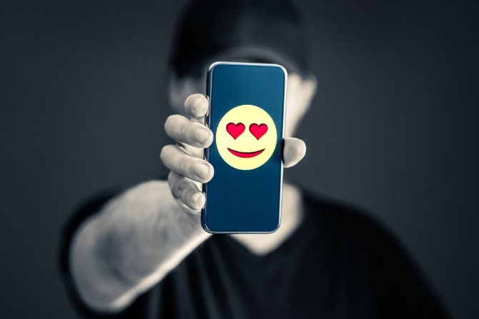 Person holding a mobile phone that’s displaying an emoji with heart eyes, indicating catfishing online
